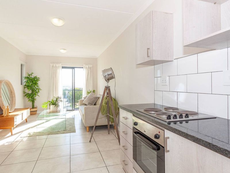 Bright open-plan living area featuring a modern kitchen with built-in oven and hob, tiled flooring, and direct access to a balcony through sliding doors.