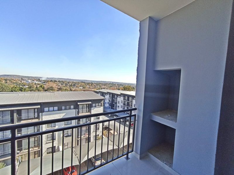 A covered balcony featuring a built-in braai, metal balustrade, and expansive views over the surrounding residential complex and landscape.