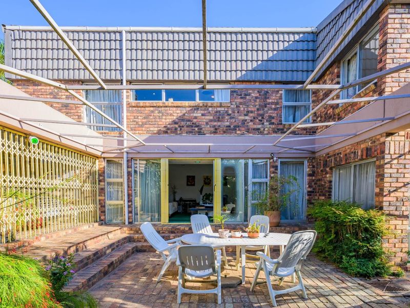 Rear exterior view featuring a paved patio area, brick facade, and a metal pergola frame, providing direct access to the interior living space.
