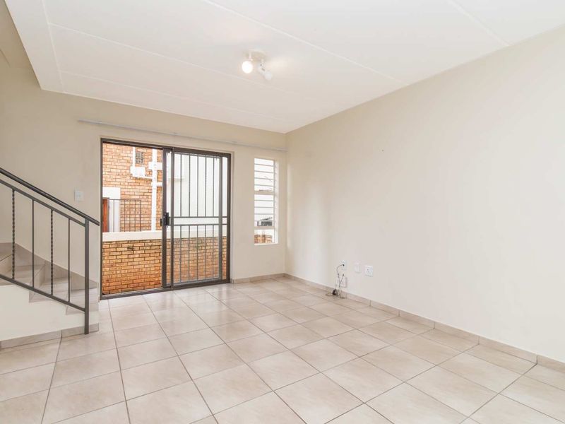 A bright, open-plan living area featuring neutral tiled flooring, a staircase with metal railing, and a sliding glass door leading to the exterior.