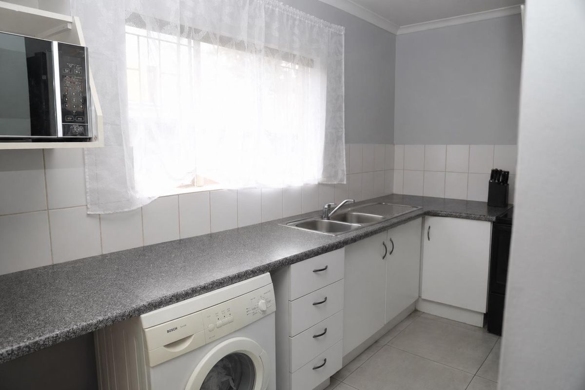 A functional kitchen featuring granite countertops, a stainless steel double sink, tiled backsplash, and ample built-in cabinetry with space for laundry appliances.