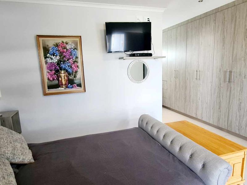 A well-maintained bedroom featuring extensive built-in cupboards with a modern wood-grain finish and neutral tiled flooring.