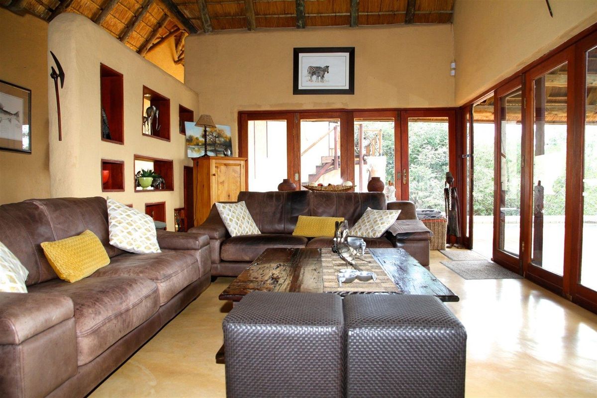 Spacious living room featuring a high thatched roof, exposed timber beams, polished concrete flooring, and large wooden-framed glass doors leading to the patio.