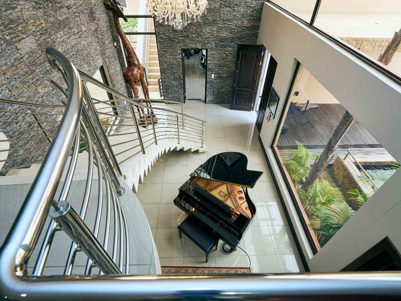 Grand double-volume entrance hall featuring a striking curved staircase with stainless steel balustrades, stone feature wall, and expansive windows overlooking the garden.
