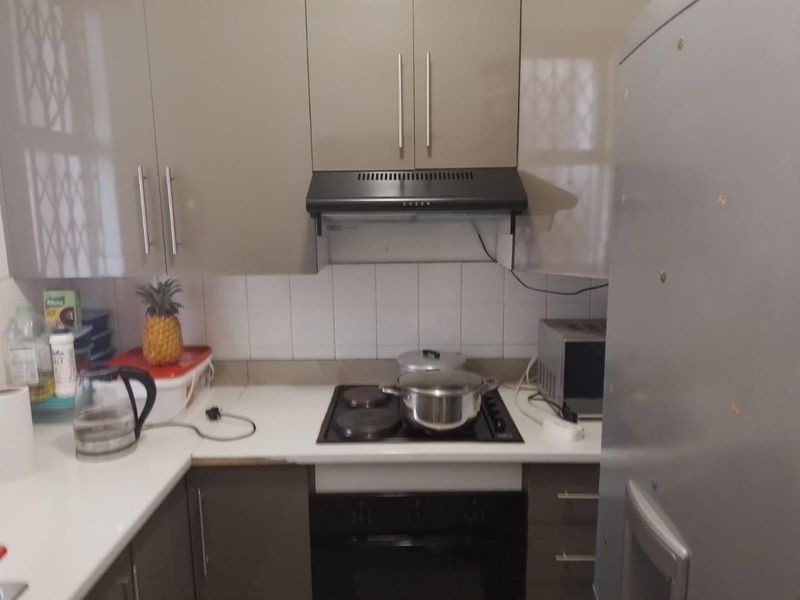 A compact kitchen featuring modern grey cabinetry, a built-in electric hob with extractor fan, and a tiled backsplash.