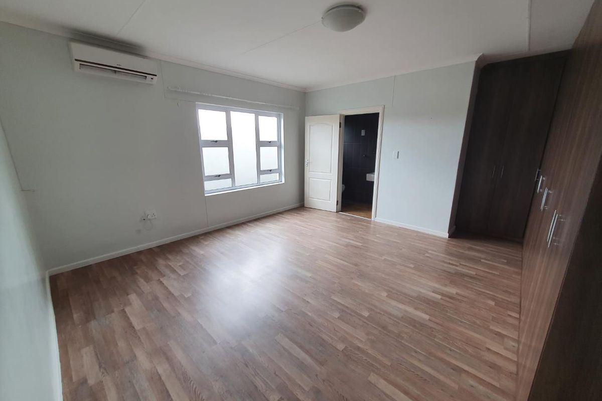 Spacious bedroom featuring wood-look laminate flooring, built-in cupboards, an integrated air conditioning unit, and an en-suite bathroom.