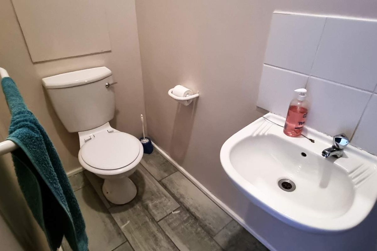 A compact office restroom featuring a wall-mounted basin with tiled splashback, a standard toilet, and wood-look floor tiling.