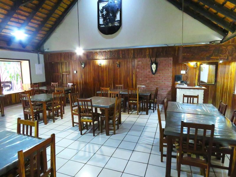 Spacious dining area featuring high vaulted ceilings with exposed timber trusses, wood-paneled walls, an exposed brick accent, and durable ceramic floor tiling.
