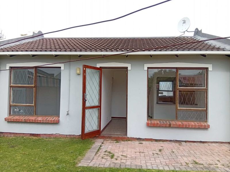 Rear exterior view of a townhouse featuring a tiled roof, paved patio area, and security-fitted windows with some visible maintenance required.