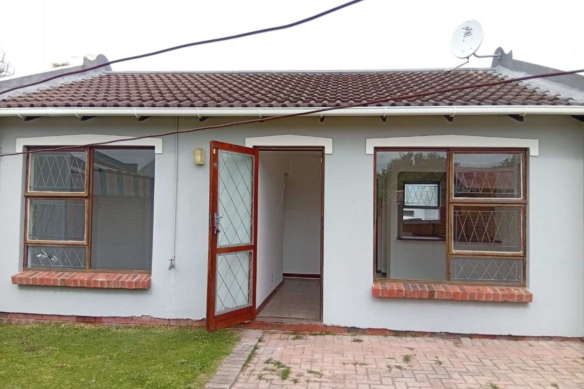 Rear exterior view of a townhouse featuring a tiled roof, paved patio area, and security-fitted windows with some visible maintenance required.