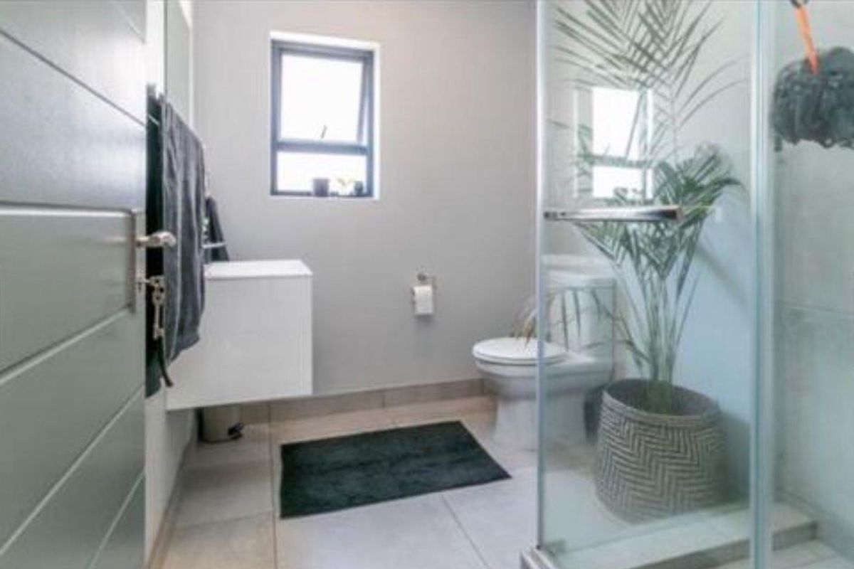 A modern bathroom featuring a wall-mounted vanity, a glass-enclosed shower, and neutral floor tiling, providing a clean and functional space.