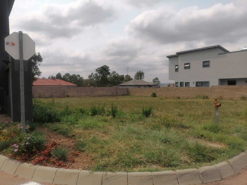 A vacant residential plot featuring a perimeter brick wall, fire hydrant, and established concrete kerbing, situated in a developed neighborhood.