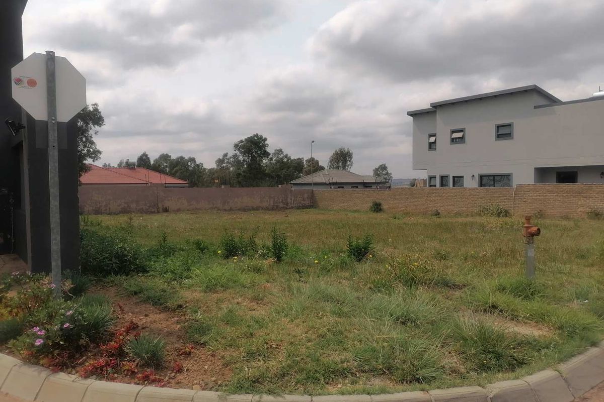 A vacant residential plot featuring a perimeter brick wall, fire hydrant, and established concrete kerbing, situated in a developed neighborhood.