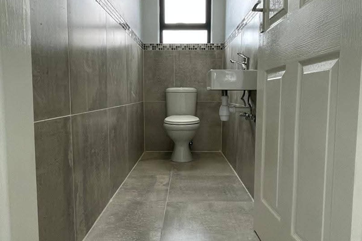 A clean, modern guest bathroom featuring neutral grey floor and wall tiles, a wall-mounted basin, and a toilet.