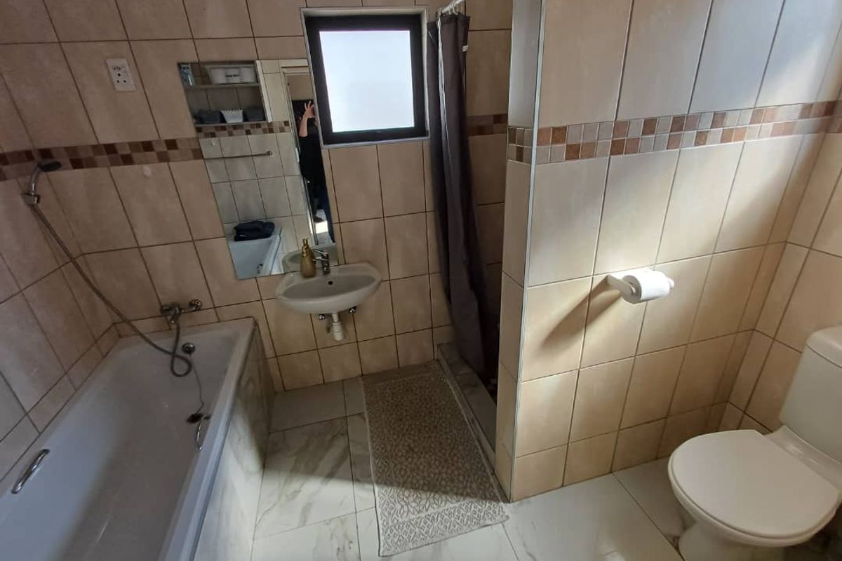 A functional bathroom featuring a bathtub with shower attachment, pedestal basin, and toilet, finished with neutral wall and floor tiling.