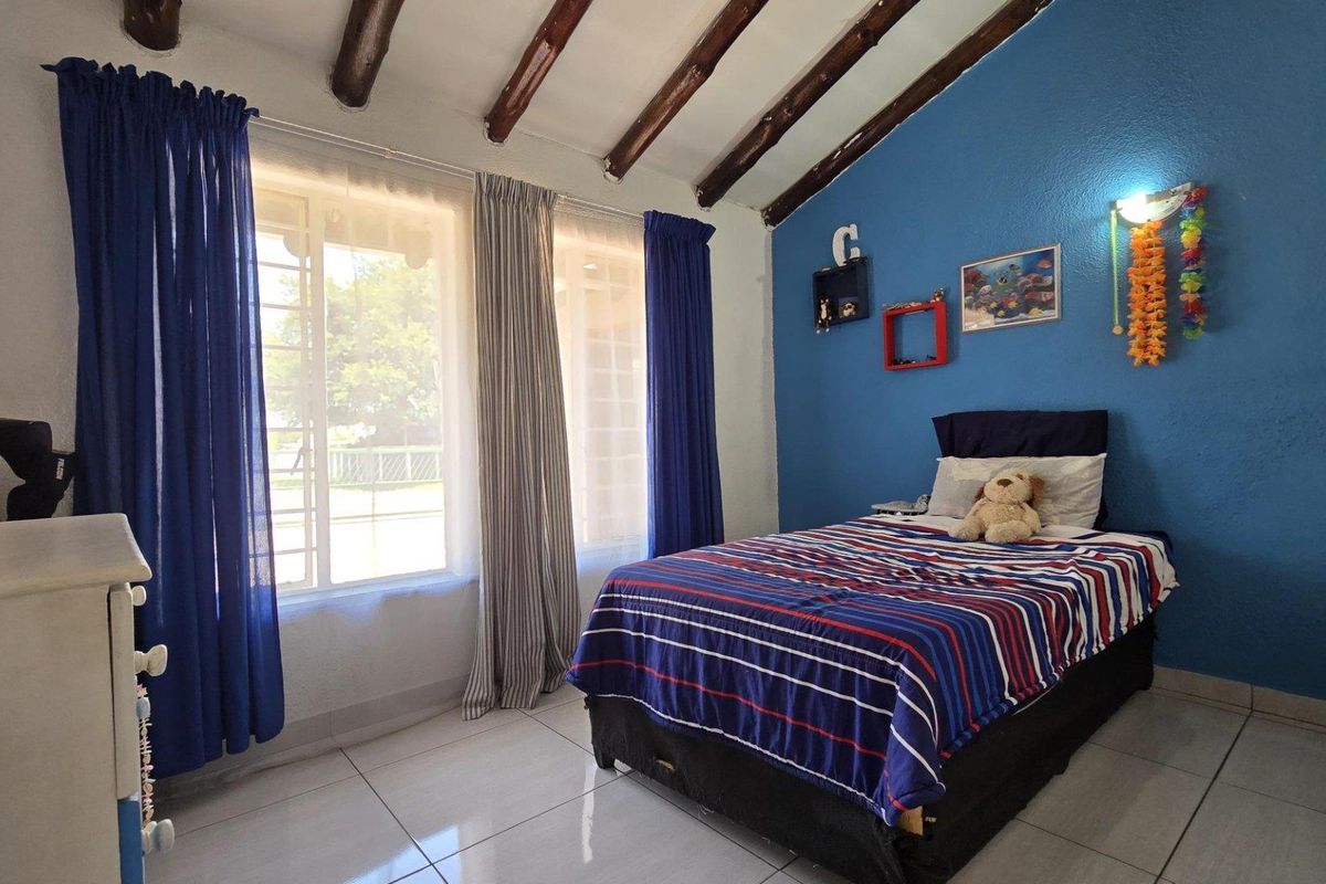 A bedroom featuring exposed timber ceiling beams, tiled flooring, and large windows that provide natural light.