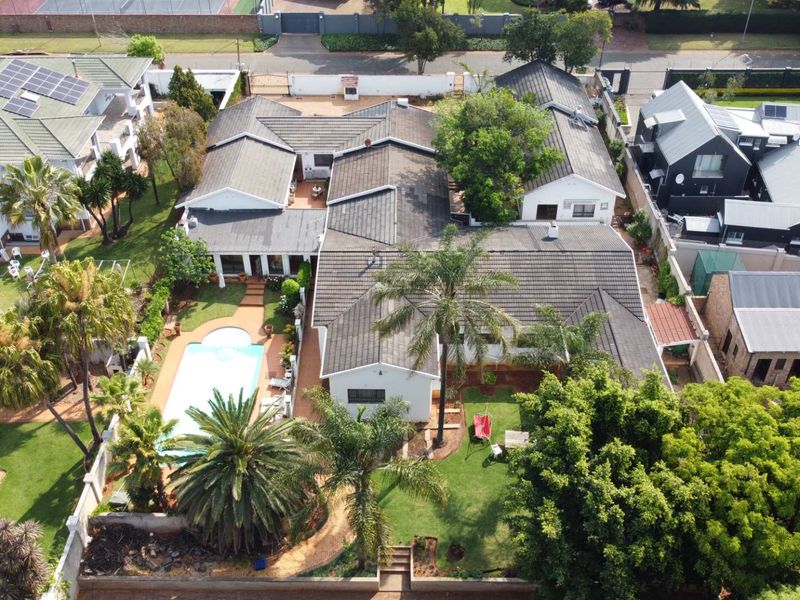 Aerial view of a residential property featuring a tiled roof, swimming pool, solar panels, and established garden areas within a secure perimeter.
