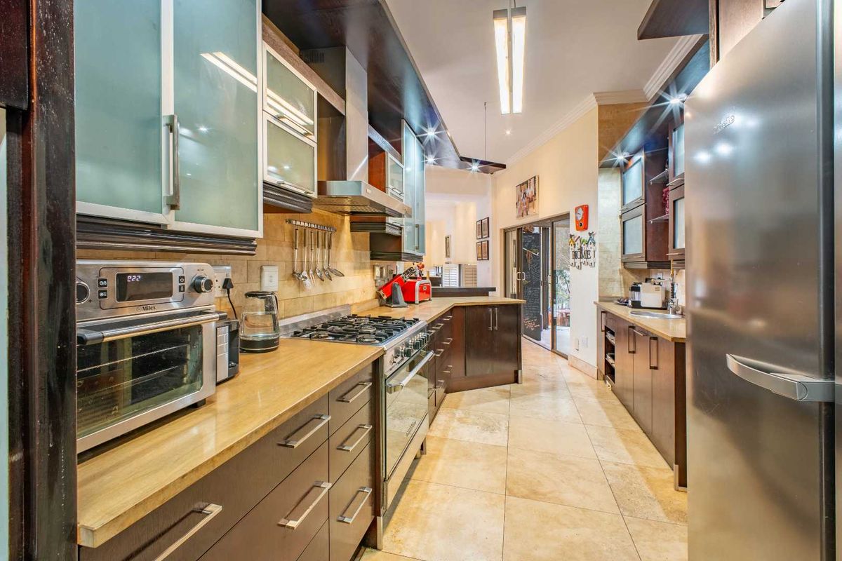 A well-appointed kitchen featuring dark cabinetry, stone countertops, a gas hob, stainless steel extractor fan, and tiled flooring, leading to an open-plan living area.