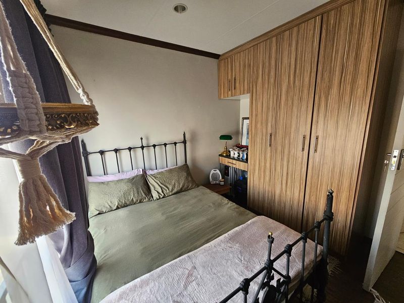 A compact bedroom featuring floor-to-ceiling wood-finish built-in wardrobes and an integrated vanity area with recessed lighting.