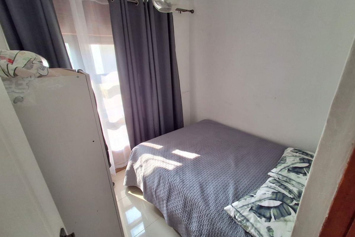 A compact bedroom featuring tiled flooring, a window with curtain treatments, and exposed brick detailing near the ceiling.