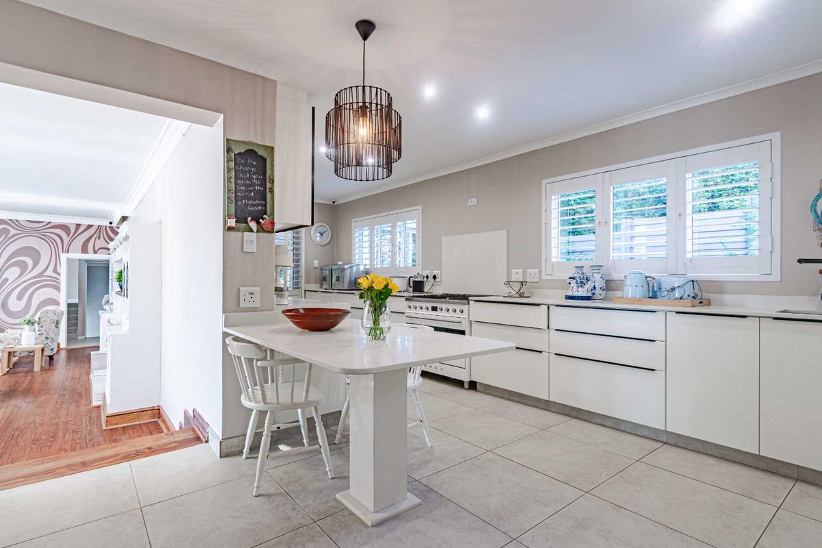 Modern kitchen featuring sleek white cabinetry, integrated breakfast island, tiled flooring, and plantation shutters, offering a bright and functional culinary space.