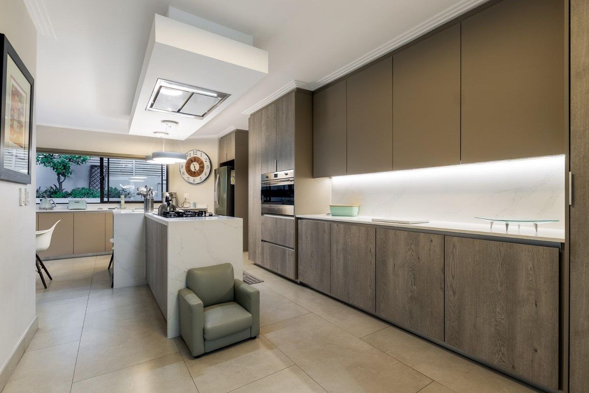 Modern kitchen featuring sleek wood-grain cabinetry, stone countertops, a central island with integrated cooktop, and built-in oven, complemented by recessed under-cabinet lighting.