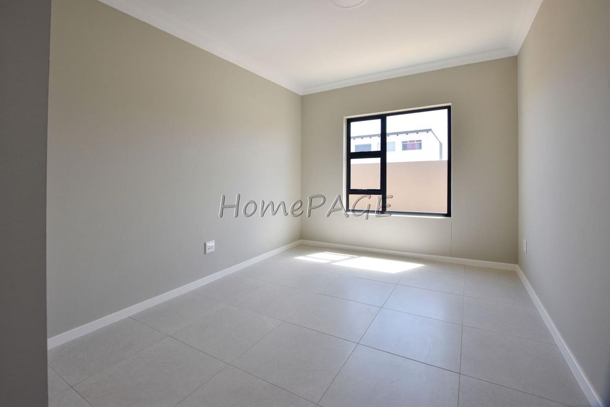 A bright, empty bedroom featuring neutral wall paint, modern tiled flooring, and a black-framed window.