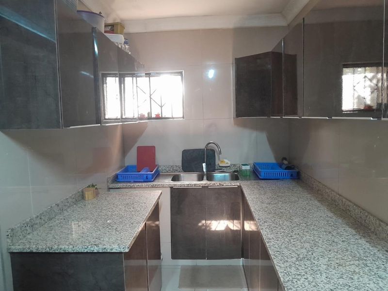 A functional kitchen featuring granite countertops, double bowl sink, and modern glossy cabinetry with ample storage space.