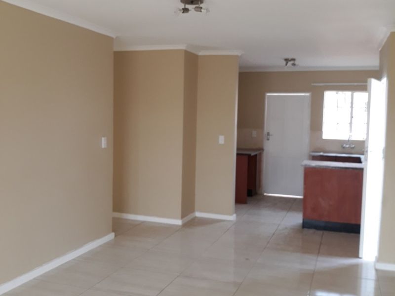 An open-plan living and kitchen area featuring neutral wall tones, tiled flooring, and built-in kitchen cabinetry with a sink.