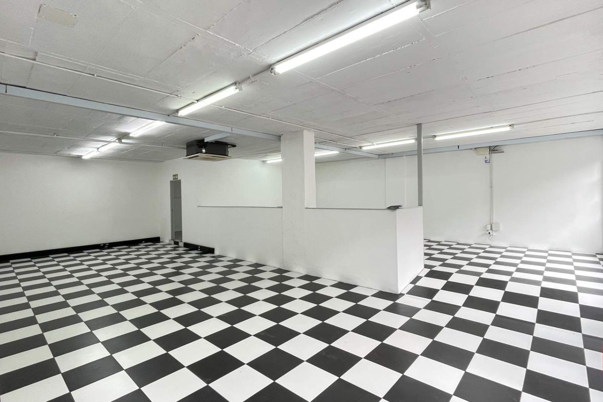 A spacious, open-plan retail area featuring high-contrast checkered flooring, bright fluorescent lighting, and a central partition wall, suitable for various commercial uses.