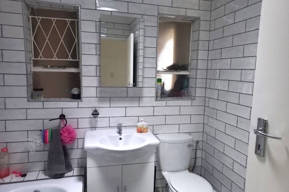 A modern bathroom featuring white subway wall tiles, a vanity basin, a toilet, and two recessed windows with security bars.
