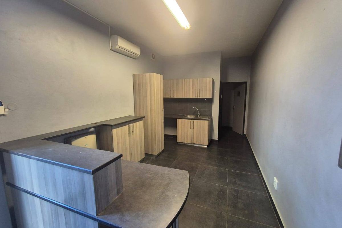 A functional kitchenette area featuring wood-look cabinetry, a stainless steel sink, dark tiled flooring, and a wall-mounted air conditioning unit.