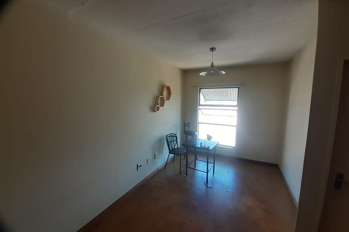 A sparsely furnished bedroom featuring a single pendant light and an awning window, with plain walls and worn flooring.