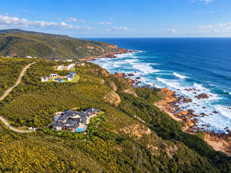An aerial view of a coastal residential property situated on a cliffside, featuring a swimming pool and scenic ocean views.