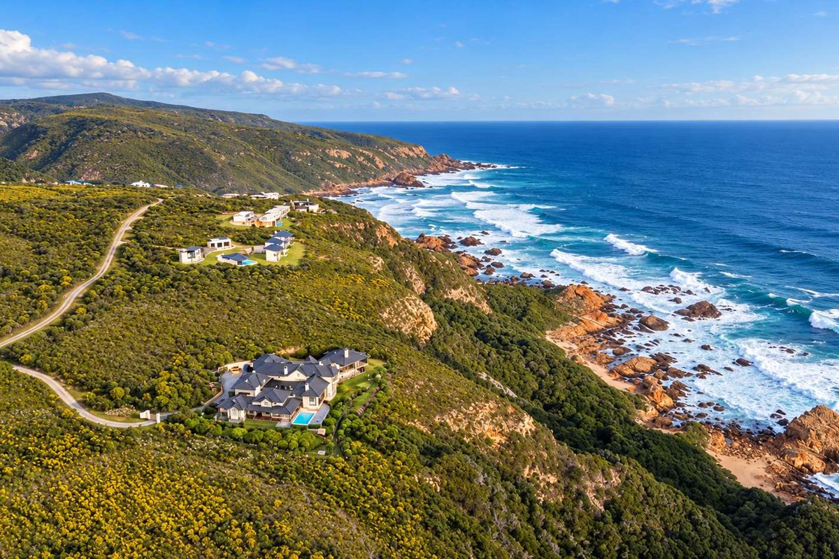 An aerial view of a coastal residential property situated on a cliffside, featuring a swimming pool and scenic ocean views.
