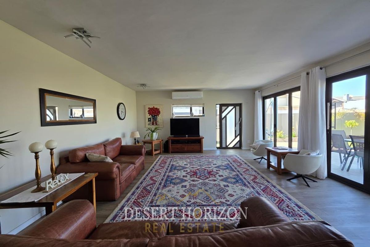 Spacious living room featuring laminate flooring, split-system air conditioning, and large sliding glass doors providing direct access to the outdoor patio area.