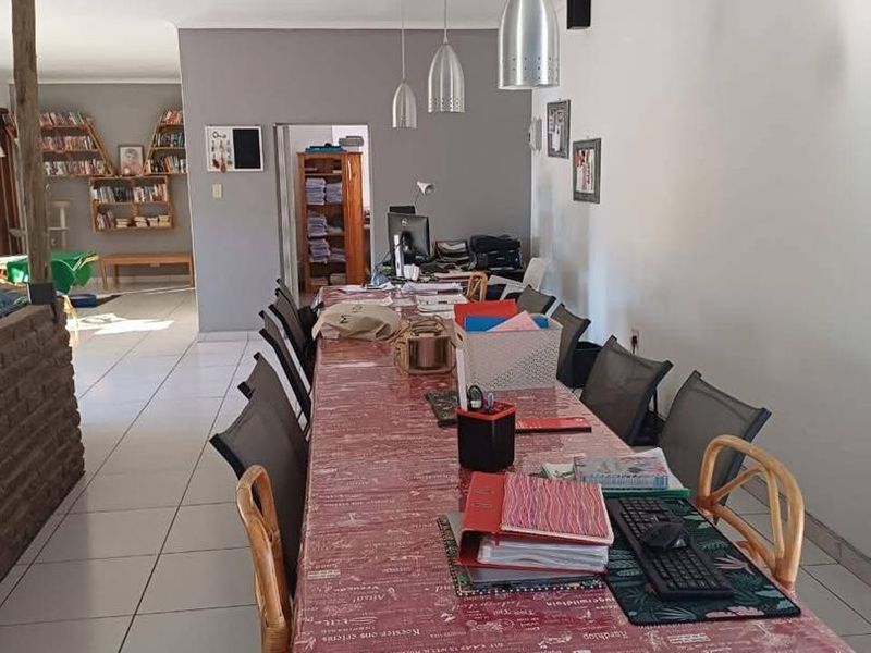 A spacious dining area featuring tiled flooring and modern pendant lighting, with built-in shelving visible in the adjacent room.