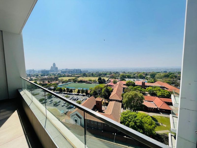 Elevated balcony view overlooking the surrounding neighborhood, school grounds, and city skyline.