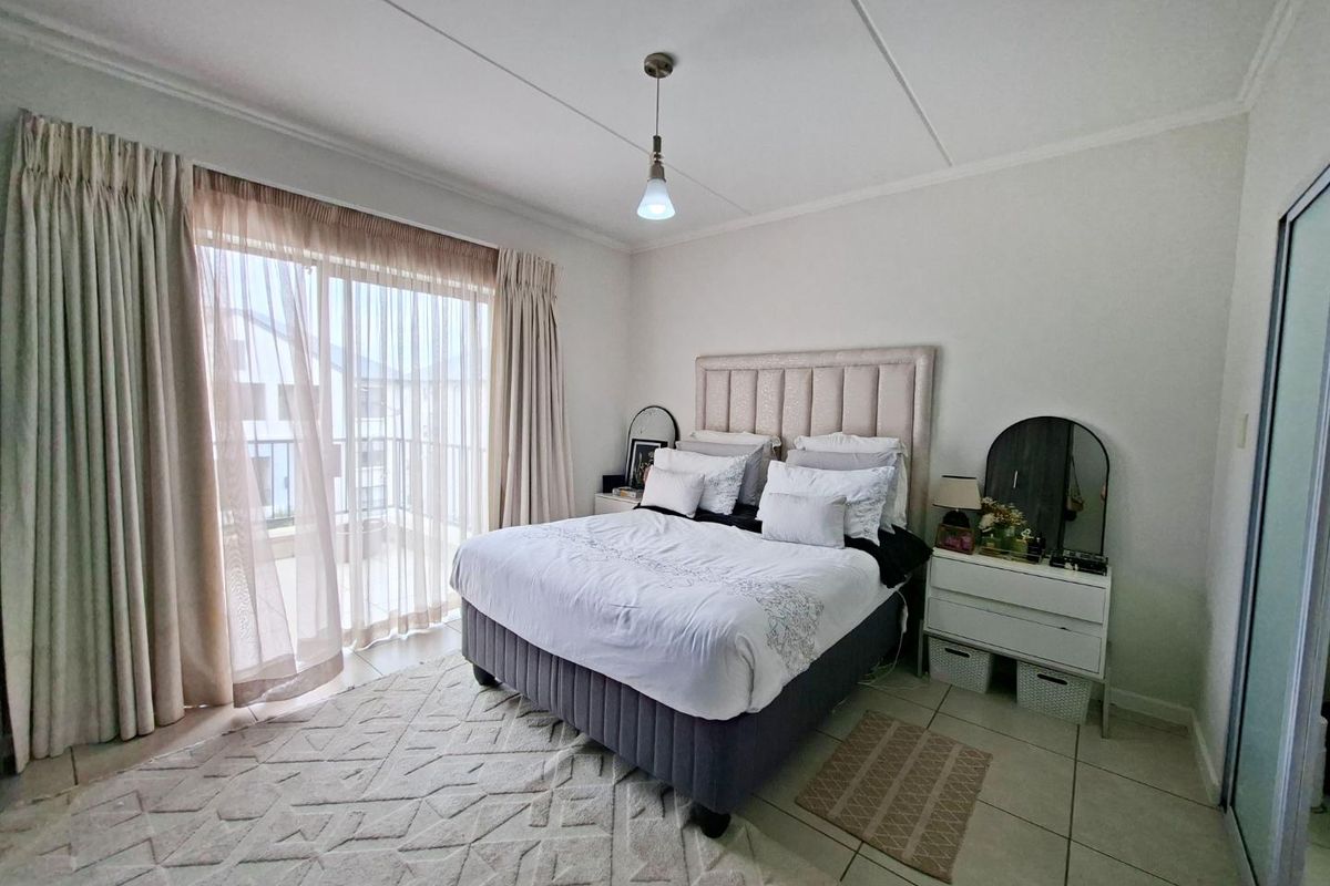 A bright bedroom featuring tiled flooring, a sliding glass door leading to a balcony, and a built-in wardrobe.