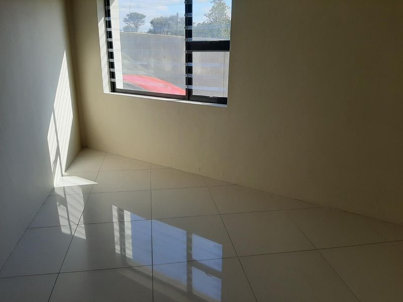A bright, empty room featuring polished ceramic floor tiles and a modern aluminium-framed louvre window, offering a clean and neutral space.