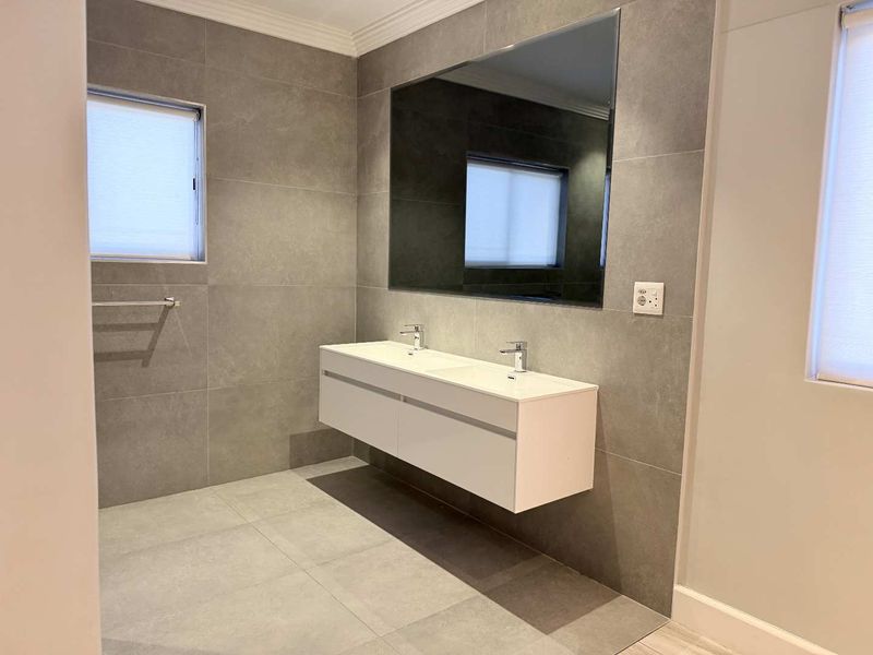 Modern bathroom featuring a sleek wall-mounted double vanity, large mirror, and contemporary grey floor-to-ceiling tiling.