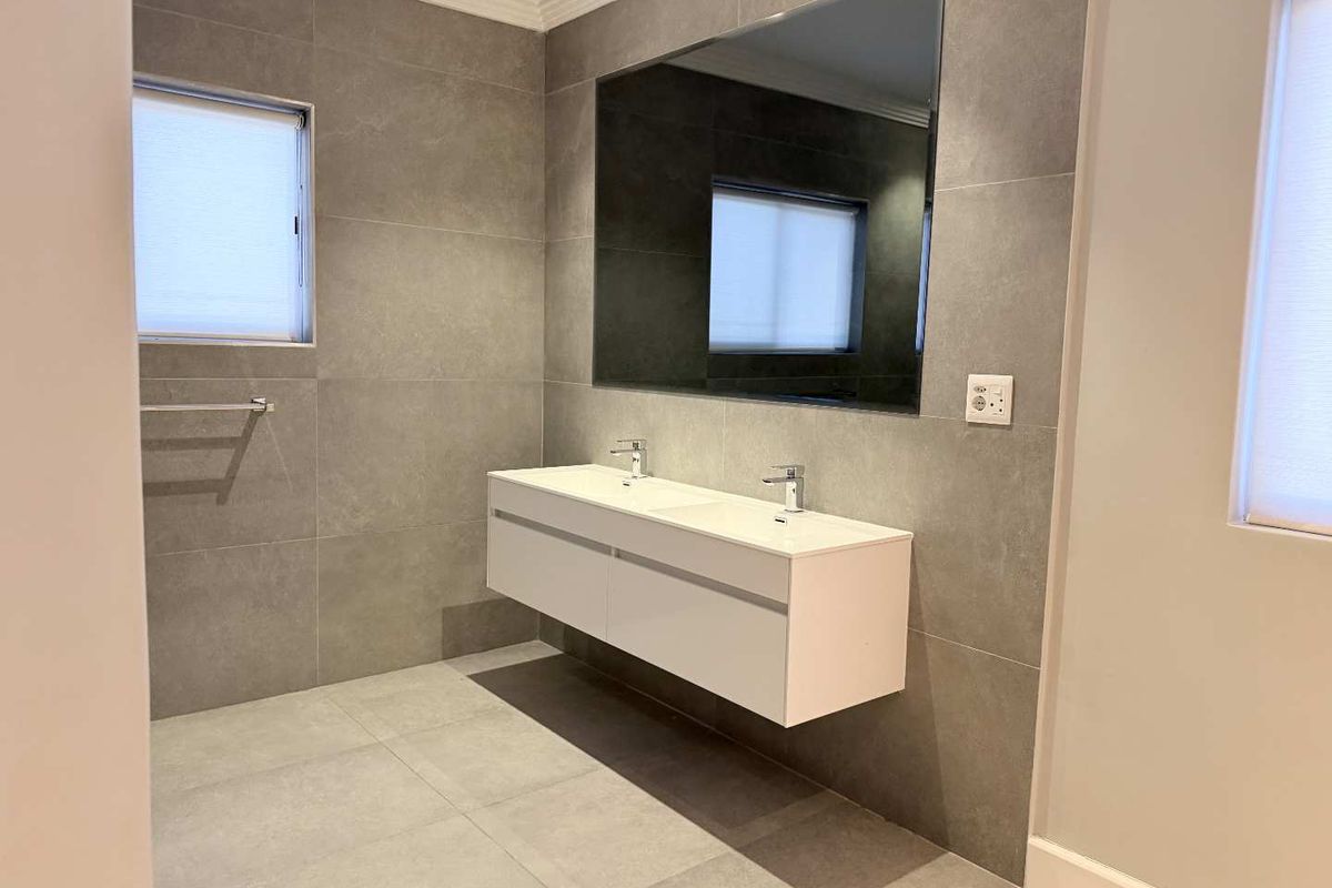 Modern bathroom featuring a sleek wall-mounted double vanity, large mirror, and contemporary grey floor-to-ceiling tiling.