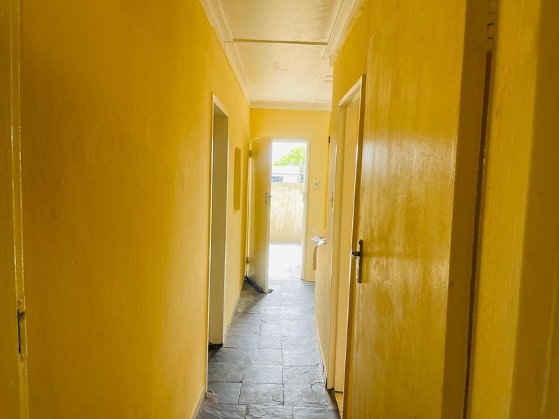 A narrow hallway featuring tiled flooring and multiple internal doorways, leading towards an exterior exit.