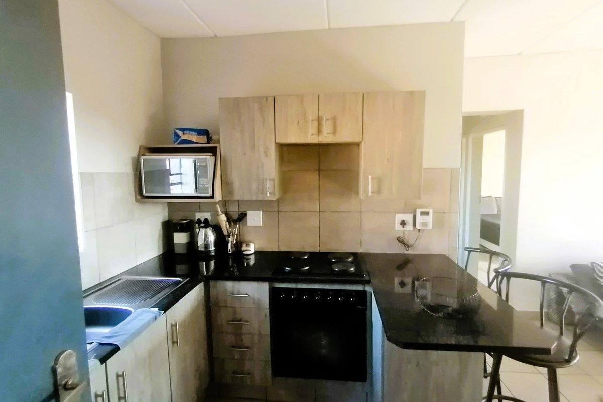 Compact kitchen featuring dark granite countertops, light wood-finish cabinetry, built-in oven, and hob, with an integrated breakfast bar area.