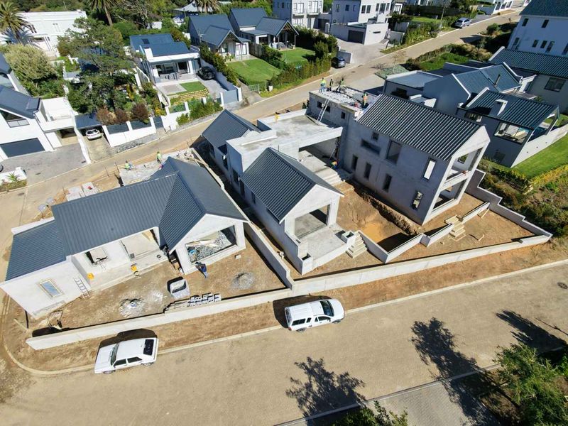 Aerial view of a residential development site showing multiple houses under construction with metal roofing and concrete structural frames.