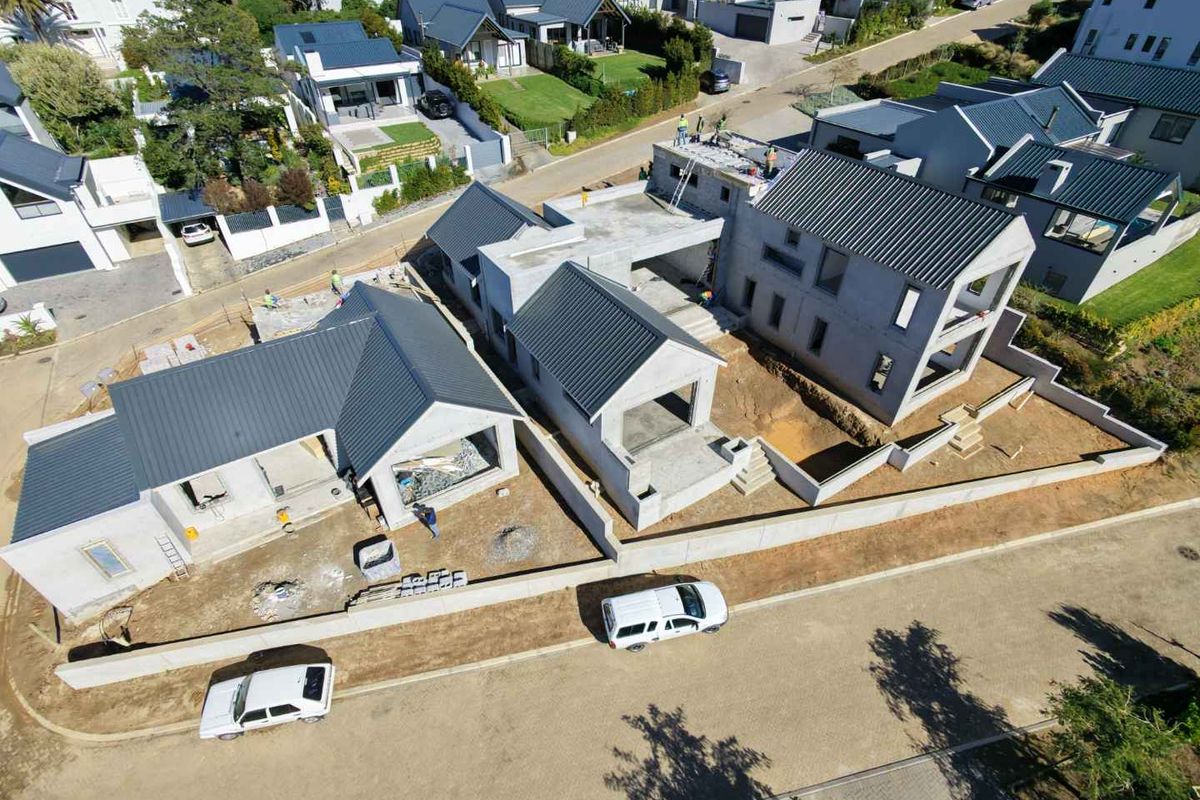 Aerial view of a residential development site showing multiple houses under construction with metal roofing and concrete structural frames.