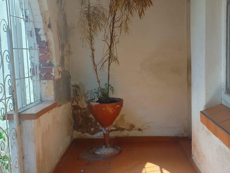 A covered patio area featuring tiled flooring and security gates, currently showing significant signs of wall surface deterioration and peeling paint.