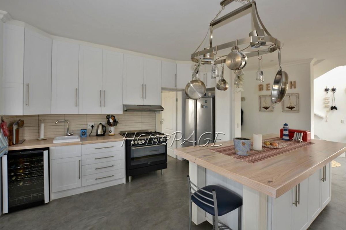Modern kitchen featuring white cabinetry, light wood countertops, a central island with breakfast bar, and a stainless steel hanging pot rack.
