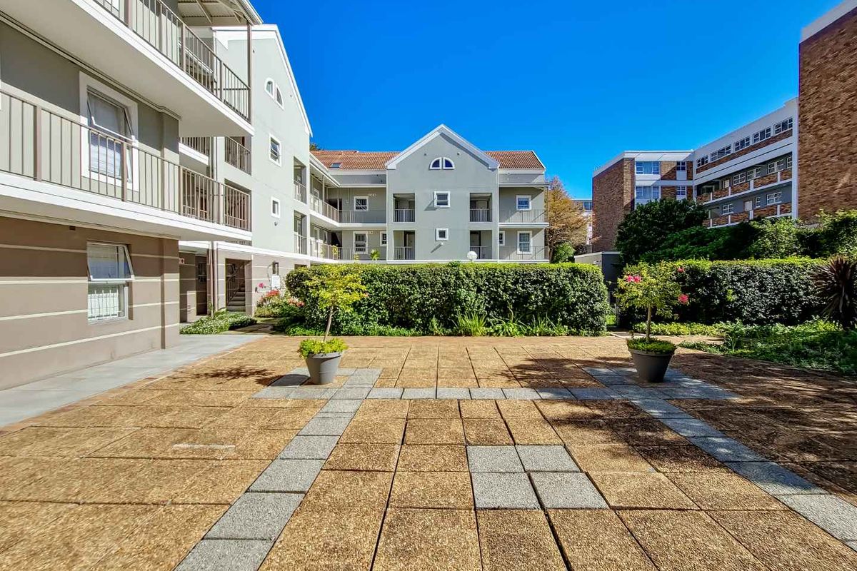 A well-maintained communal courtyard area featuring paved surfaces, landscaped hedging, and views of the surrounding apartment building facades.