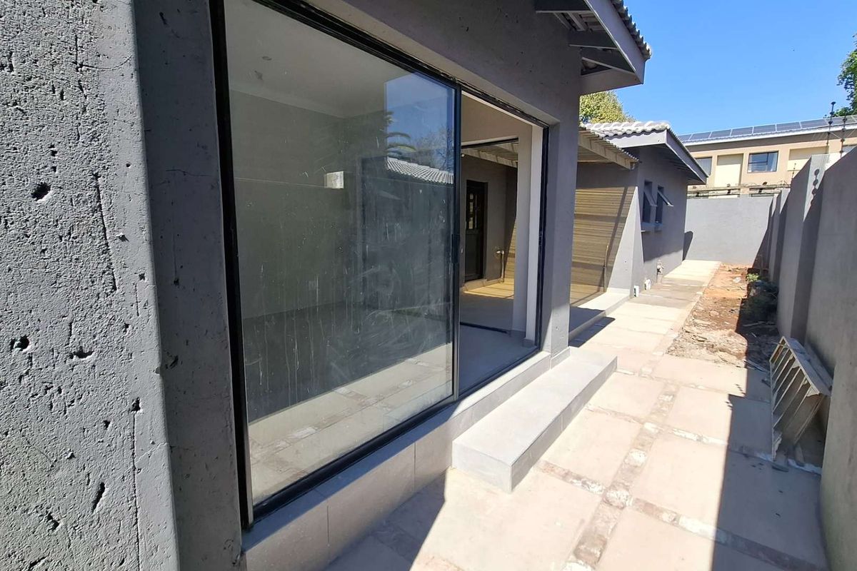 Rear exterior view showing a sliding glass door entrance, concrete paved walkway, and boundary wall with unfinished garden area.